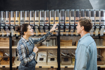 Shop assistant helping customer in bulk food store. Seller advising woman in her purchase of...