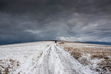 Dirt road leading to the top of the hill at wintertime, dramatic storm clouds, passing horse chariot, focus on the road.