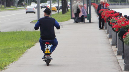 A man rides on a sitting electric scooter on the paved Nagatinskaya embankment road of the Moscow River on a summer day, personal city transport