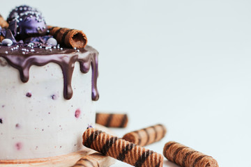  Purple glitter blueberry cake with chocolate glaze on a white background copy space. Homemade chocolate cake with blueberries and striped wafer rolls.