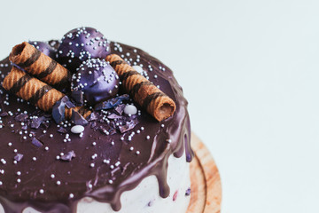  Purple glitter blueberry cake with chocolate glaze on a white background copy space. Homemade chocolate cake with blueberries and striped wafer rolls.