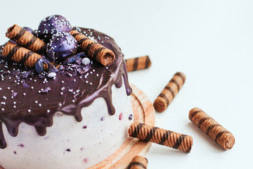  Purple glitter blueberry cake with chocolate glaze on a white background copy space. Homemade chocolate cake with blueberries and striped wafer rolls.