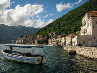 Fototapeta na wymiar view of the city of Perast in the Bay of Kotor with a boat in the foreground, mountains, blue sky and white clouds