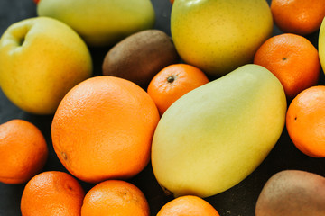 Tangerines, apples, oranges, kiwi and mangoes on a dark gray background. Orange and green fruits. Fruit diet.