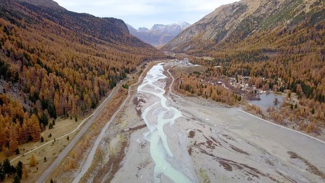 drone flight over the ova da Bernina river near Morteratsch station in Graub&uuml;nden in the Swiss alps in an autumnal landscape with yellow larches and no sun