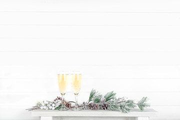 Mock up of a white wall in a room with a shelf, spruce branches and glasses of champagne