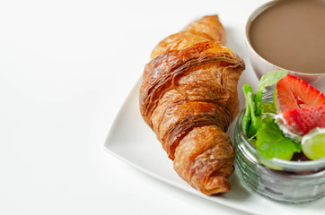 Delicious croissant on a plate with coffee in a cup and a set of fresh fruit