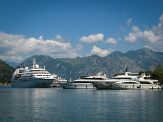 Fototapeta na wymiar white ship and yachts in the port against the backdrop of mountains and blue sky in the port of Kotor, Montenegro