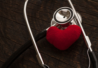 A doctor's stethoscope with red heart on wood background
