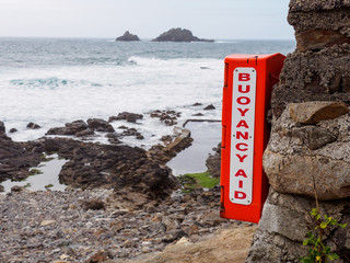 Wide closeup of a box containing a buoyancy aid, also known as a life preserver or personal flotation device, along the beach of Priest's Cove. Cornwall, United Kingdom. Swimming and safety. - 312219717