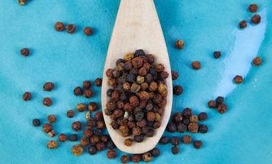 Close up of isolated wood spoon with red and black cambodian kampot pepper corns on blue old scratched china dish