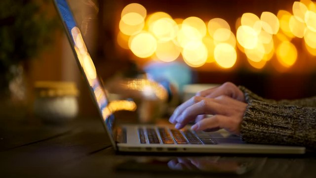 Woman wearing wool sweater typing fast with her fingers on her laptop, writing an article online and doing her job. Home celebration environment. Sliding shot, 4K
