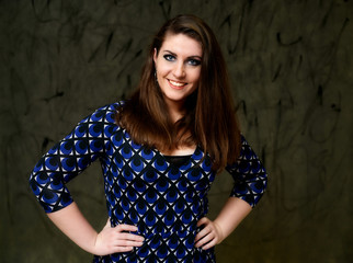 Portrait of a pretty brunette woman with a beautiful hairstyle and with excellent makeup in a dark blue blouse on a gray alternative background. Standing with a smile in front of the camera.