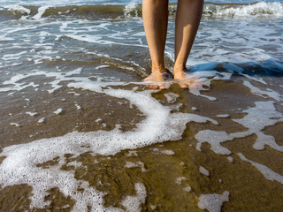 Woman legs in sea water. Closeup of woman legs on sea shore. Summer, beach, leisure and body part concept - closeup of woman legs on sea shore
