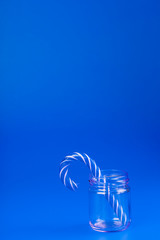 One Lollipop Candy cane in a glass jar on a blue background.