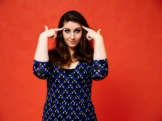 Portrait of a pretty brunette woman with a beautiful hairstyle and with excellent makeup in a dark blue blouse on a red background. He stands with a smile and shows his hands with emotions.