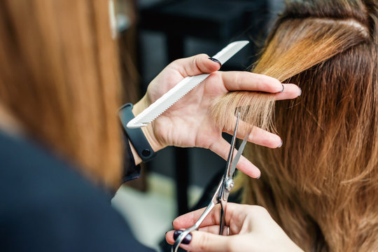 Female hairdresser is holding in hand between fingers a red hair is cutting woman hair close up.