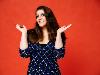 Portrait of a pretty brunette woman with a beautiful hairstyle and with excellent makeup in a dark blue blouse on a red background. He stands with a smile and shows his hands with emotions.