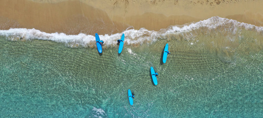 Aerial drone ultra wide photo of surfers practising with their surf boards in tropical exotic sandy bay with turquoise sea