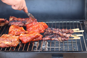 Assorted delicious grilled meat with beef stick and beef steak on black stove with smoke. grills some kind of marinated meat and vegetable on gas grill during summer party time. 