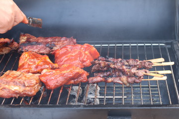 Assorted delicious grilled meat with beef stick and beef steak on black stove with smoke. grills some kind of marinated meat and vegetable on gas grill during summer party time. 