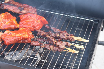 Assorted delicious grilled meat with beef stick and beef steak on black stove with smoke. grills some kind of marinated meat and vegetable on gas grill during summer party time. 