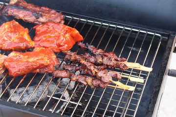 Assorted delicious grilled meat with beef stick and beef steak on black stove with smoke. grills some kind of marinated meat and vegetable on gas grill during summer party time. 