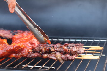 Assorted delicious grilled meat with beef stick and beef steak on black stove with smoke. grills some kind of marinated meat and vegetable on gas grill during summer party time. 
