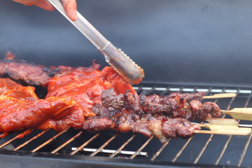 Assorted delicious grilled meat with beef stick and beef steak on black stove with smoke. grills some kind of marinated meat and vegetable on gas grill during summer party time. 