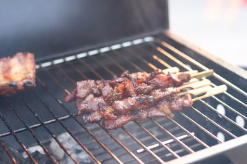 Assorted delicious grilled meat with beef stick and beef steak on black stove with smoke. grills some kind of marinated meat and vegetable on gas grill during summer party time. 