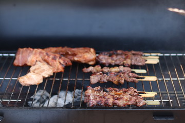 Assorted delicious grilled meat with beef stick and beef steak on black stove with smoke. grills some kind of marinated meat and vegetable on gas grill during summer party time. 