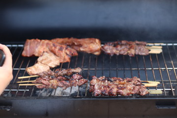 Assorted delicious grilled meat with beef stick and beef steak on black stove with smoke. grills some kind of marinated meat and vegetable on gas grill during summer party time. 
