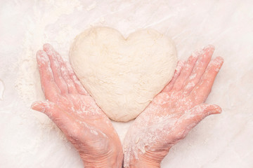 Womens hands, flour and dough. A woman is preparing a dough for home baking. Holding a heart shaped dough in his hands. concept of home cooking, baking at home.