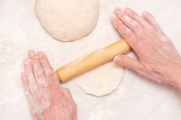 Womens hands, flour and dough. A woman is preparing a dough for home baking. Rolls out the dough with a wooden rolling pin. concept of home cooking, baking at home.