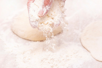 Womens hands, flour and dough. A woman is preparing a dough for home baking. Flour the dough and table. concept of home cooking