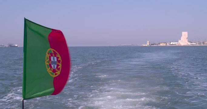 Portuguese flag waving at the wind on the back of a boat. Belem tower on the background. Shot in slow motion.