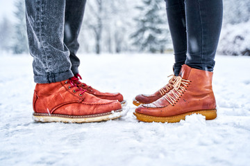 Feet of a couple on a snowy sidewalk in brown boots. The couple is standing opposite each other. Winter weather concept