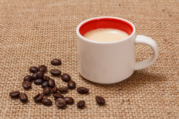 Cup of coffee and roasted coffee beans on sackcloth.