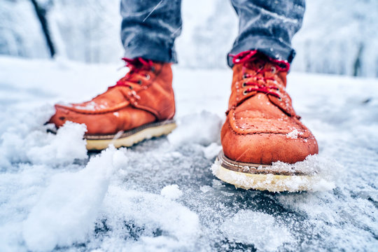 Feet Of A Man On A Snowy Sidewalk In Brown Boots. Winter Slippery Pawement. Seasonal Weather Concept