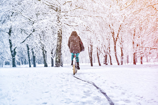 Woman rides a bicycle in a snowfall in a park. Seasonal weather concept