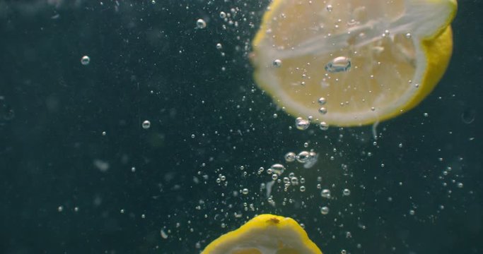 Several lemon fruits fall inside a water tank and disturb water. Three bright yellow lemon fruits fall inside a water tank and return to the surface.