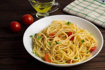 Spaghetti with tomatoes and micro-greens on a dark wooden background.