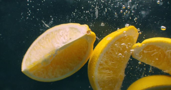 Several lemon fruits fall inside a water tank and disturb water. Three bright yellow lemon fruits fall inside a water tank and return to the surface.