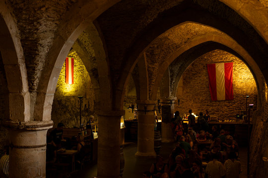 Vianden, Luxembourg: Interior stays of the medieval castle of Vianden, during medieval fair in summer. Underground cellars with vaulted ceiling and pointed arches on columns. Dim lights.