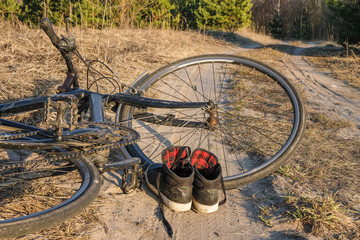 Fototapeta na wymiar Bicycle and shoes on a sandy road in a forest in Ukraine. Travel Adventure. Lifestyle.