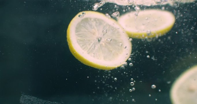 Several lemon fruits fall inside a water tank and disturb water. Three bright yellow lemon fruits fall inside a water tank and return to the surface.