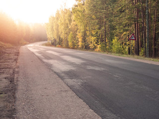 Empty asphalt road in a forest. New surface without marking, Warm sunny day, Nobody. Sun flare.