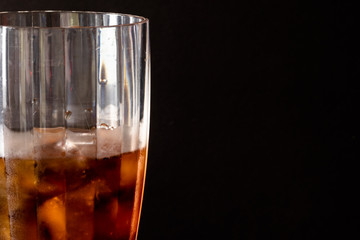 partial view of a cola soda glass with ice and sweaty glass on black background. Text space