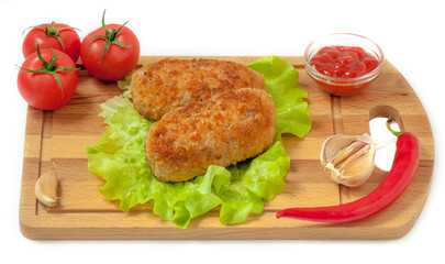 Fried cutlets on the leaves of lettuce on a cutting board on a white background, surrounded by tomato, red pepper, ketchup and garlic.