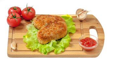 Fried cutlets on the leaves of lettuce on a cutting board on a white background, surrounded by tomato, ketchup and garlic.